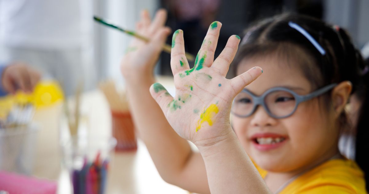 Young girl with a disability with paint on one hand and a paint brush in the other
